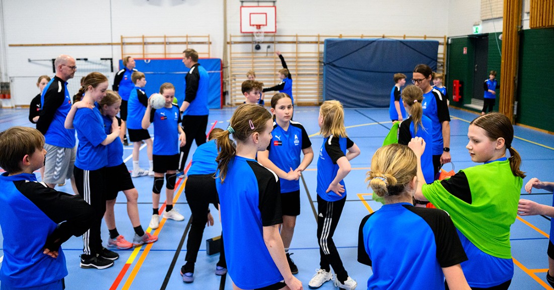 Ett lag med unga personer i blåa tröjor som står i en idrottshall