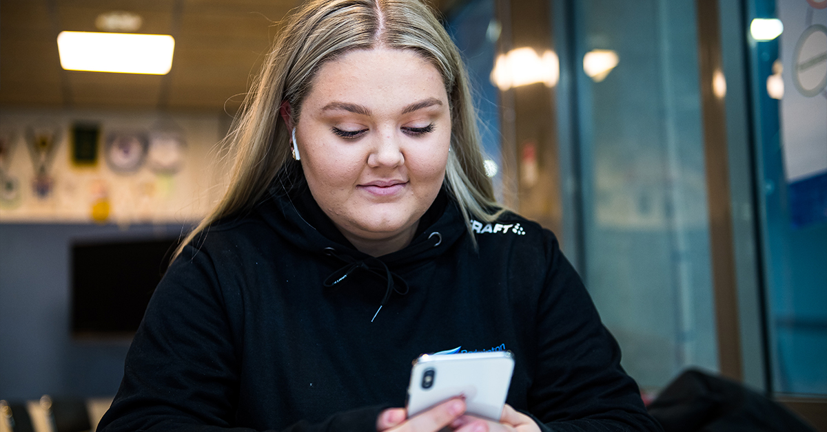Ung kvinna tittar ner på sin mobiltelefon